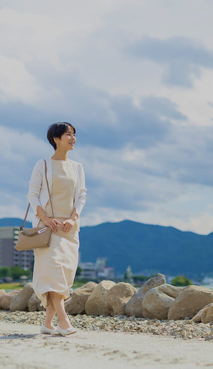 湖畔の遊歩道を笑顔で歩く女性と背景に広がる山並みと空